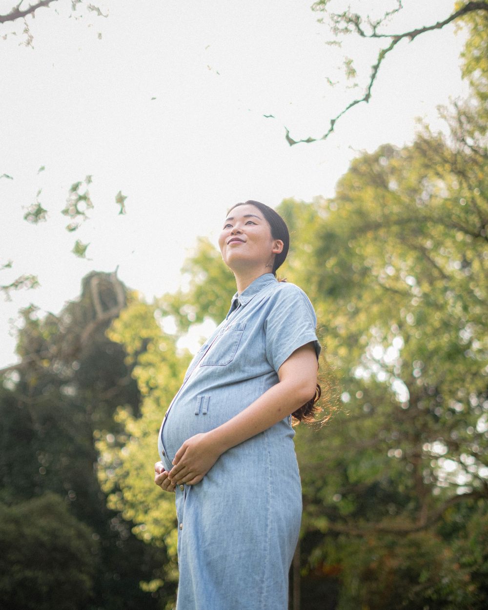 Person wearing a light blue dress poses outdoors with a hand on their belly.