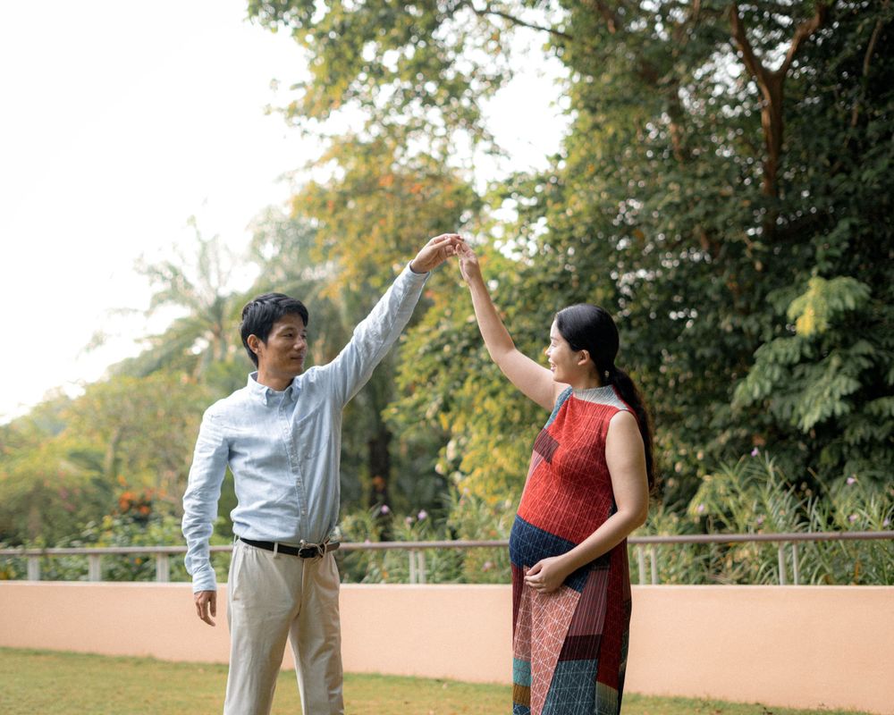 Two people dance together in a garden setting with raised arms.