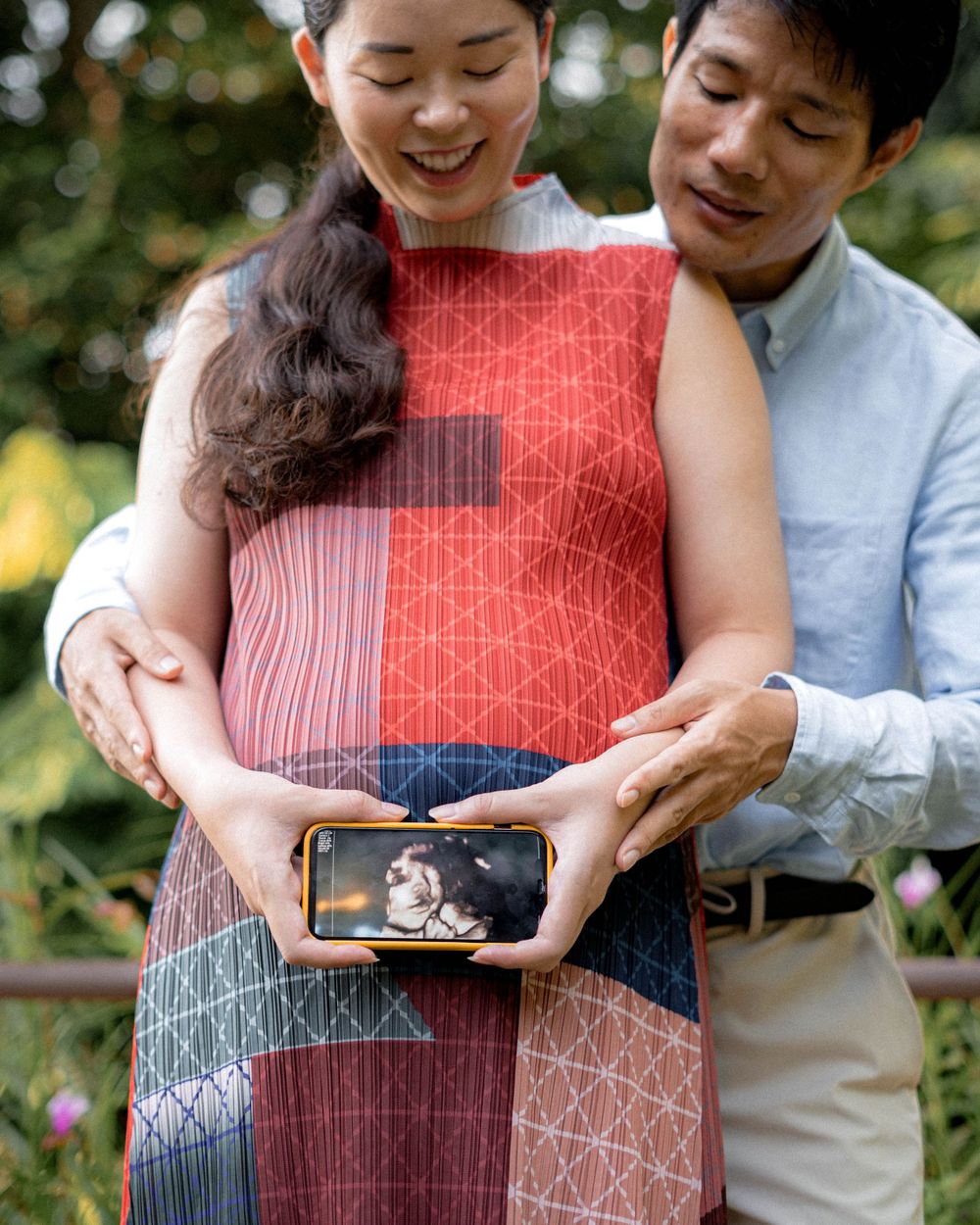 A couple holds a smartphone displaying an ultrasound image while standing outdoors.