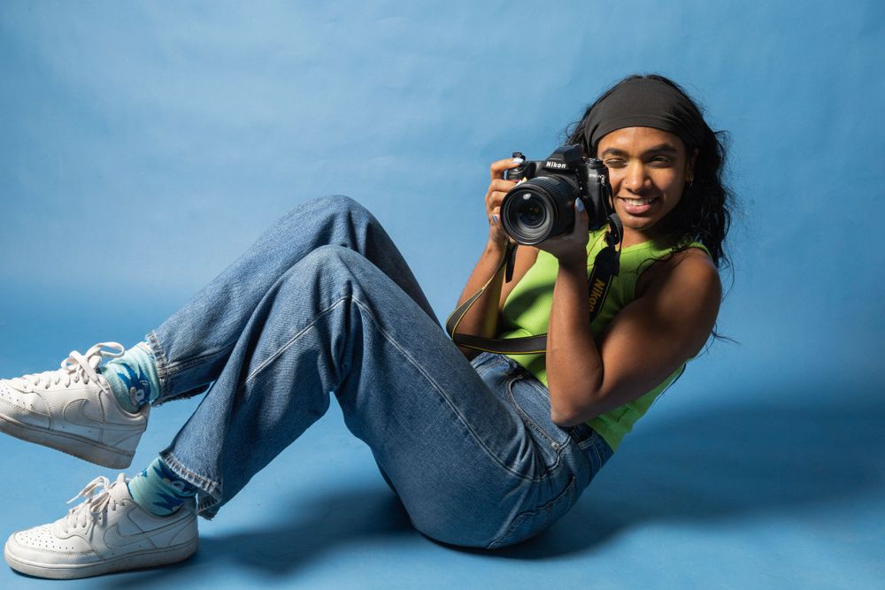 Casual portrait of photographer in jeans and green top lying down with camera.