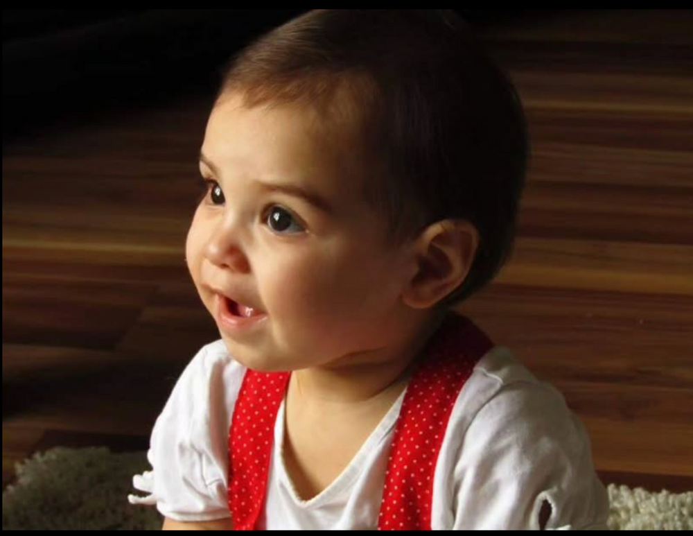 Adorable toddler in white and red polka dot outfit smiling in warm lighting.