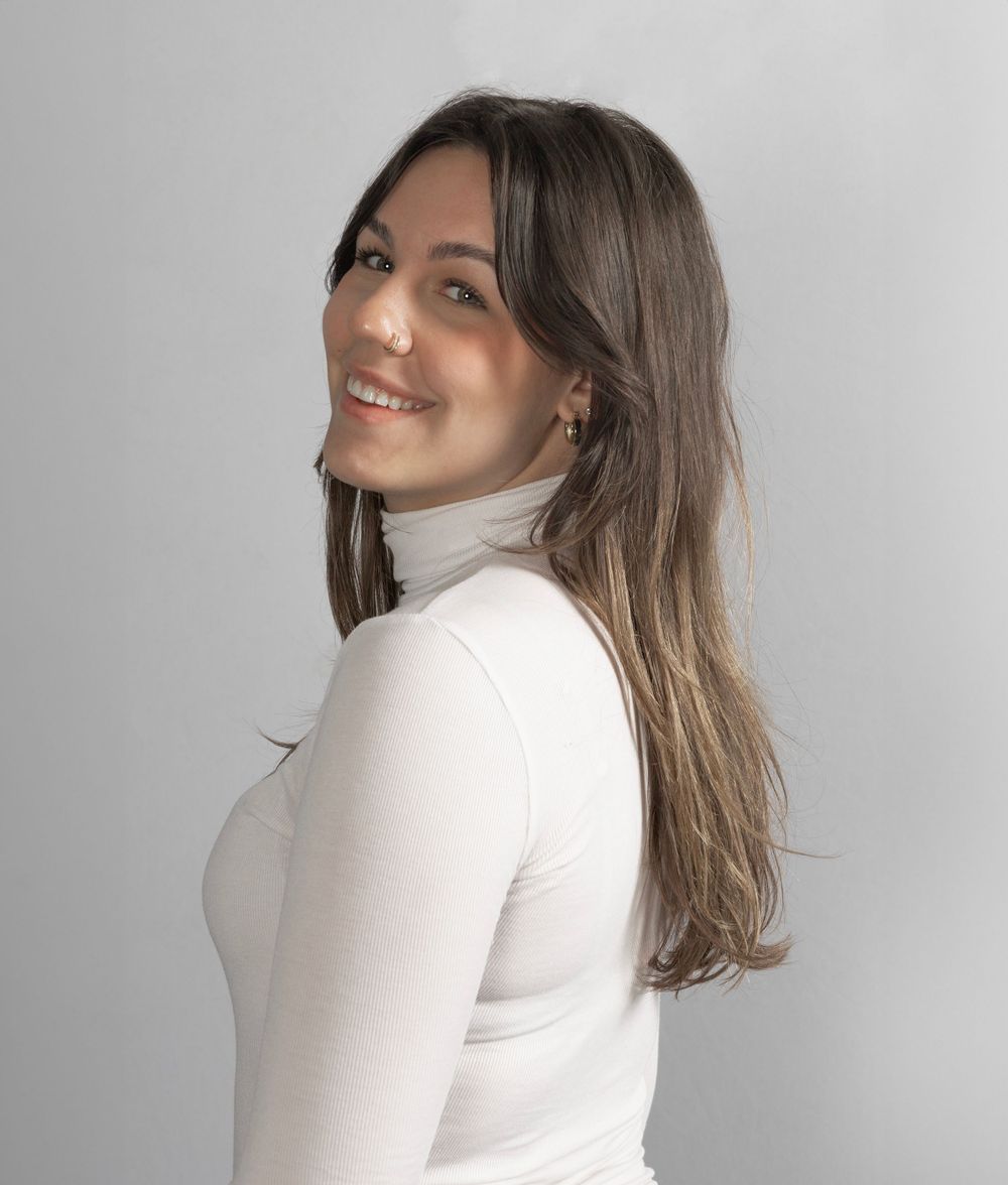 Portrait of someone in white turtleneck smiling over shoulder against light grey background.