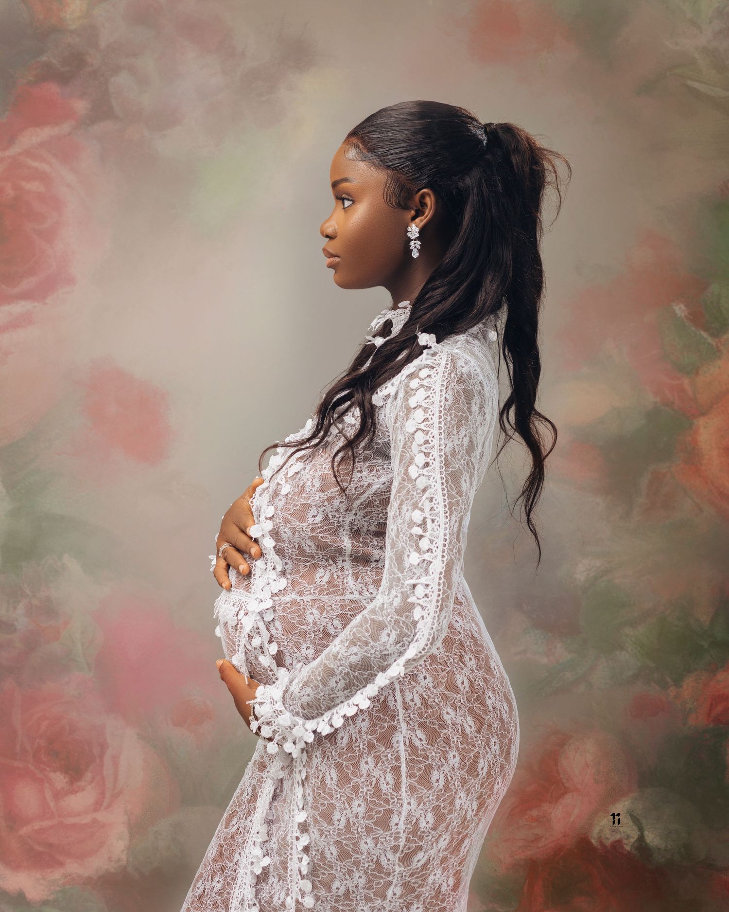 Beautiful maternity portrait in a white lace gown against a dreamy rose-colored background with soft floral elements.