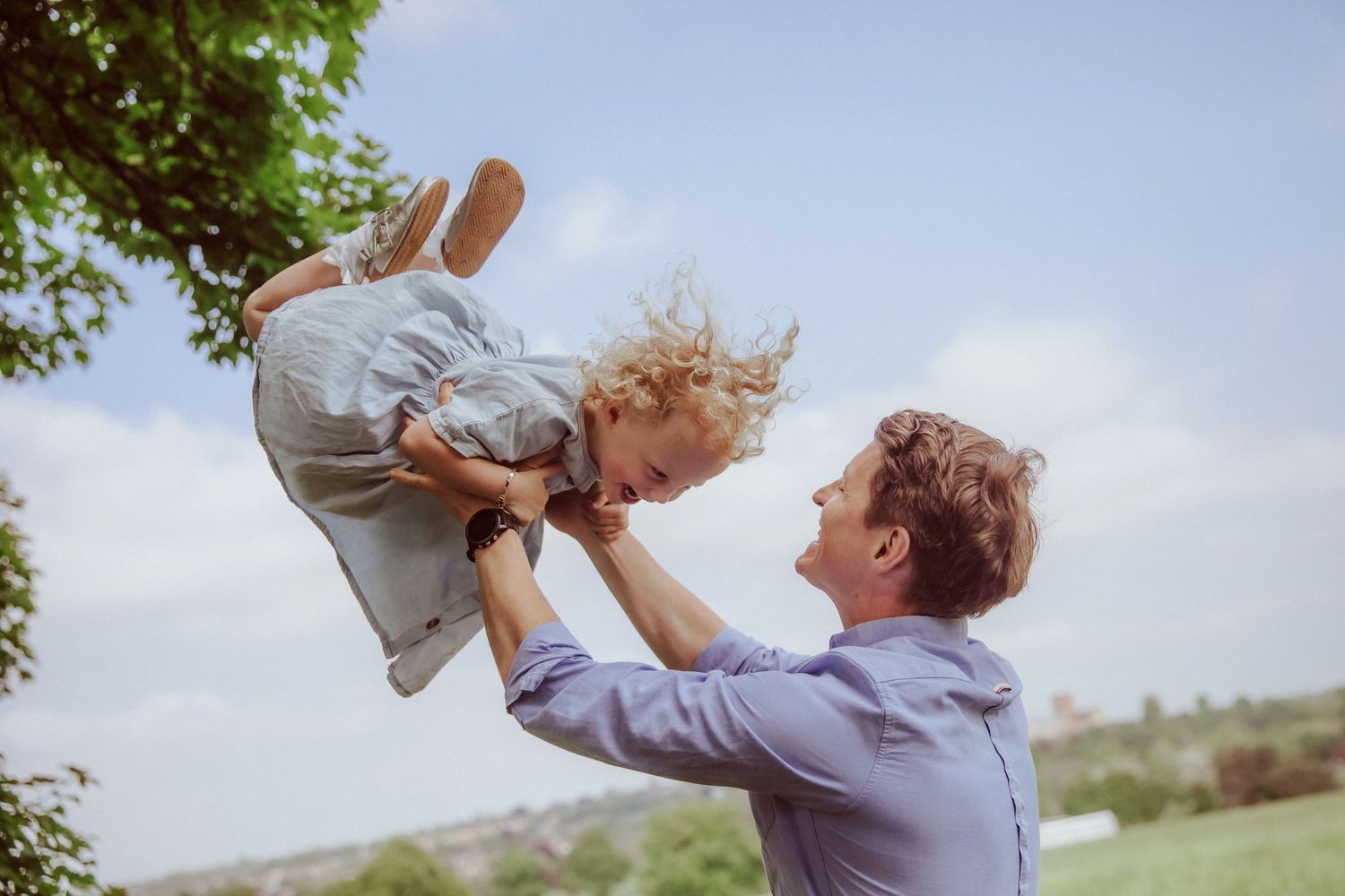 A playful moment captured outdoors shows someone lifting a child into the air during a sunny day.