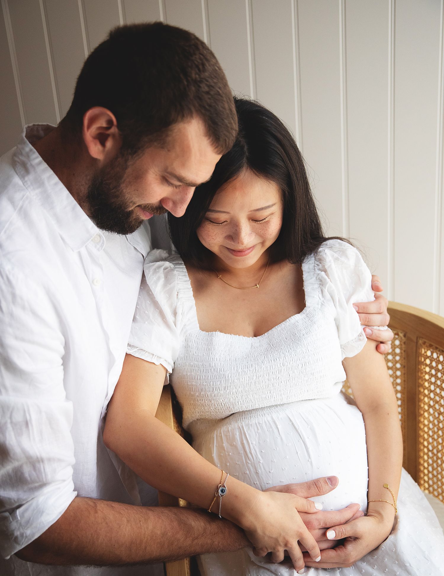Expecting couple shares an intimate moment as they lovingly embrace and touch her pregnant belly in a sunlit room. At a photoshoot in Bexley