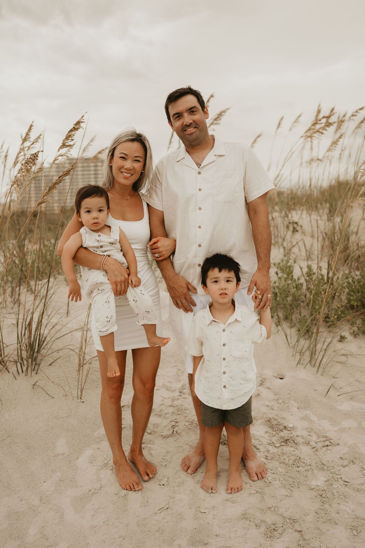 Smiling family of four posing outdoors for a family portrait during golden hour open the beach!