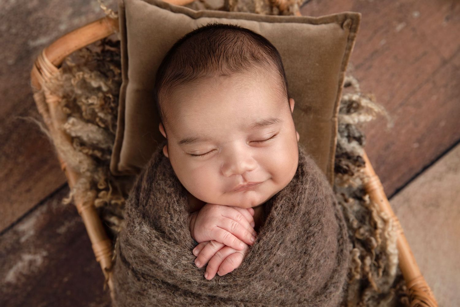 Peaceful sleeping baby wrapped in brown knit blanket on rustic wooden chair.