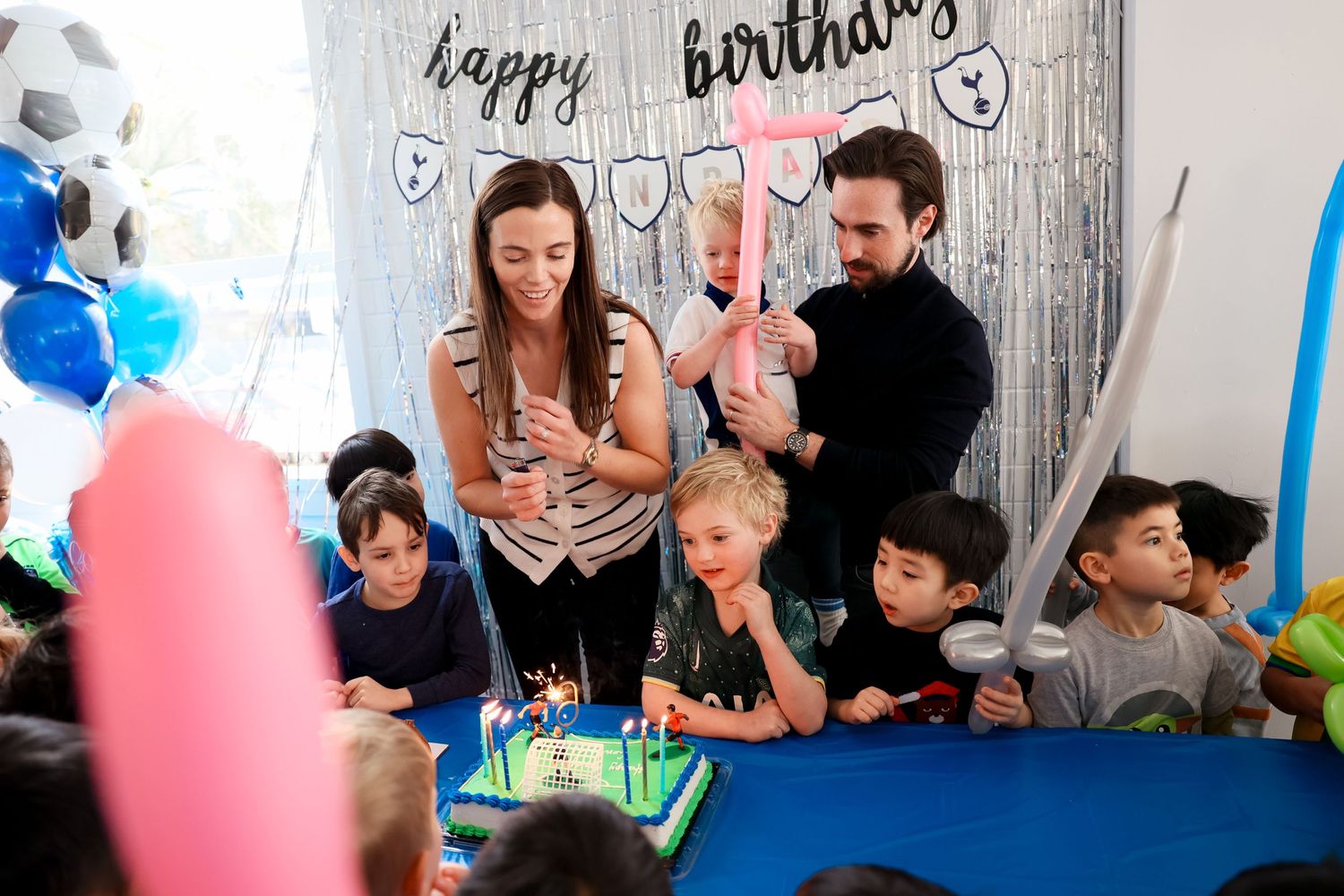 Children gathered around a birthday cake with blue and pink decorations and balloons at a festive birthday celebration by smilein.
