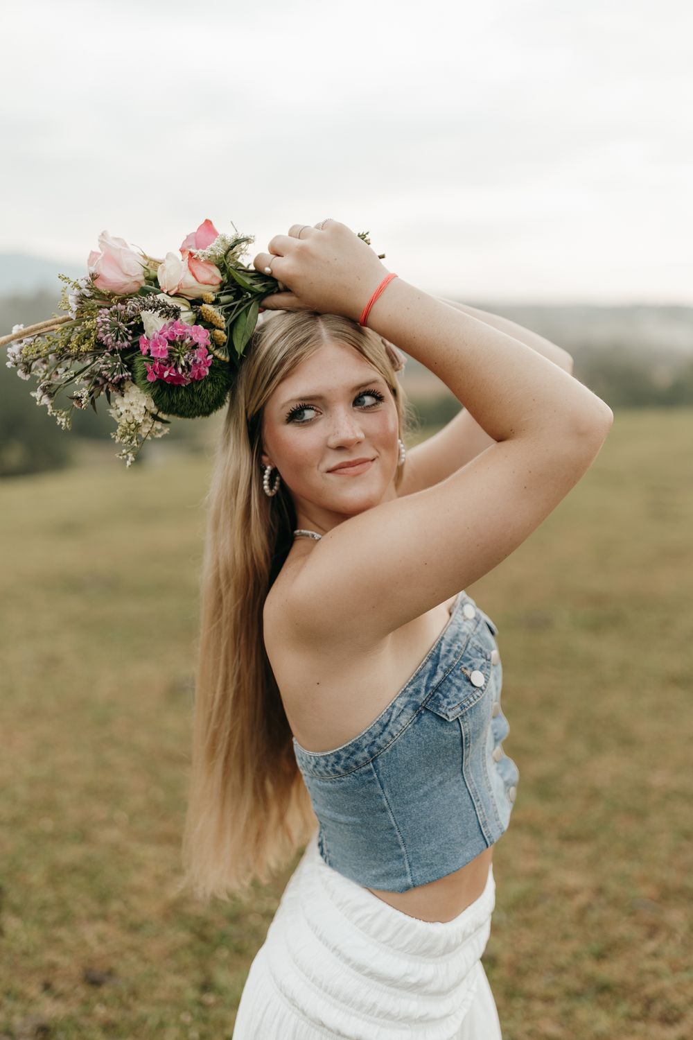 Boho-style outdoor portrait with a floral bouquet and denim crop top against a pastoral landscape. Virginia graduation/senior session.