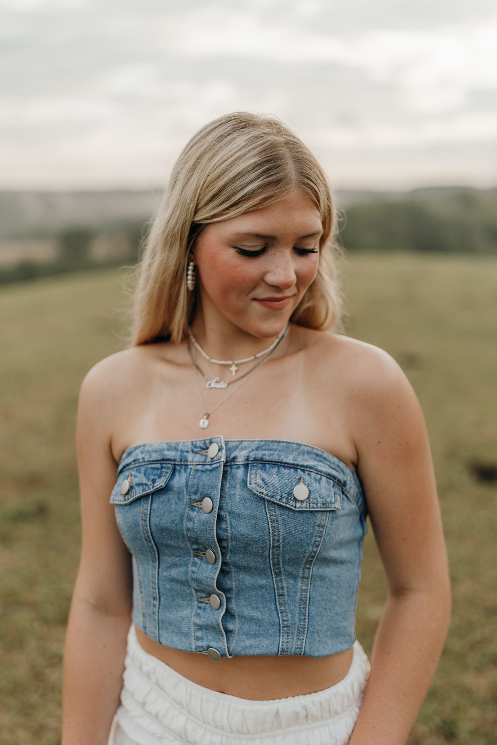 Close-up portrait showcasing a denim button-up crop top and layered necklaces against a pastoral backdrop. Virginia graduation/senior sessio