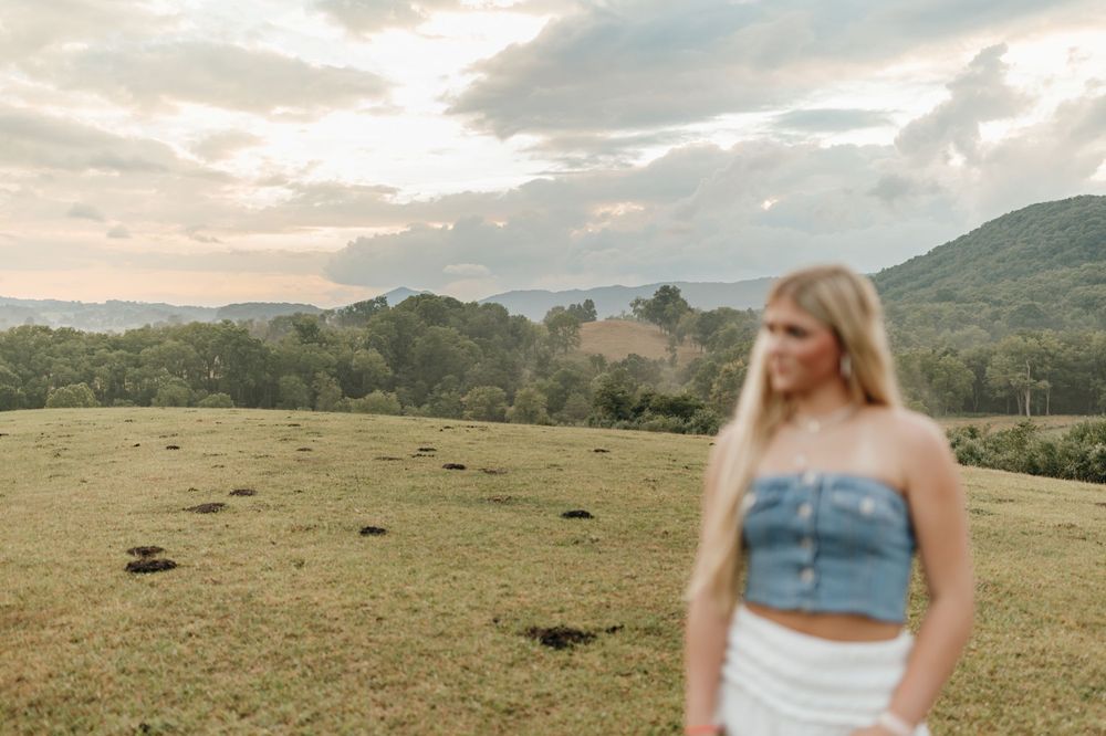 Scenic sunset photo in mountain meadow with person in denim top and white skirt. Virginia graduation/senior session.