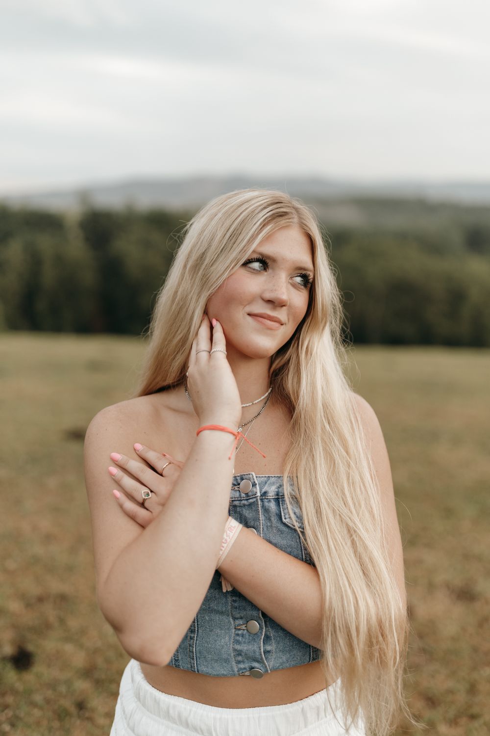 Outdoor portrait in a field showing person in denim crop top with long blonde hair against rolling hills landscape. Virginia graduation/seni