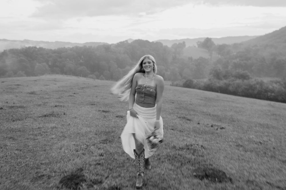 Black and white photo of person running joyfully through a hilltop meadow.  Virginia graduation/senior session.