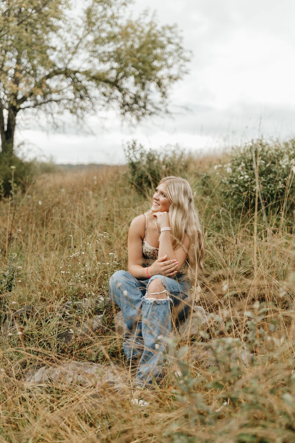 A contemplative portrait in a rustic field with golden grasses and autumn trees in the background. Virginia graduation/senior session.
