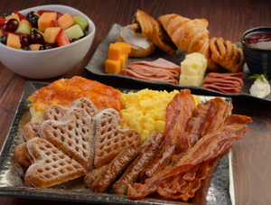 Breakfast platter with Mickey-shaped waffles, scrambled eggs, bacon, and fresh fruit bowl.