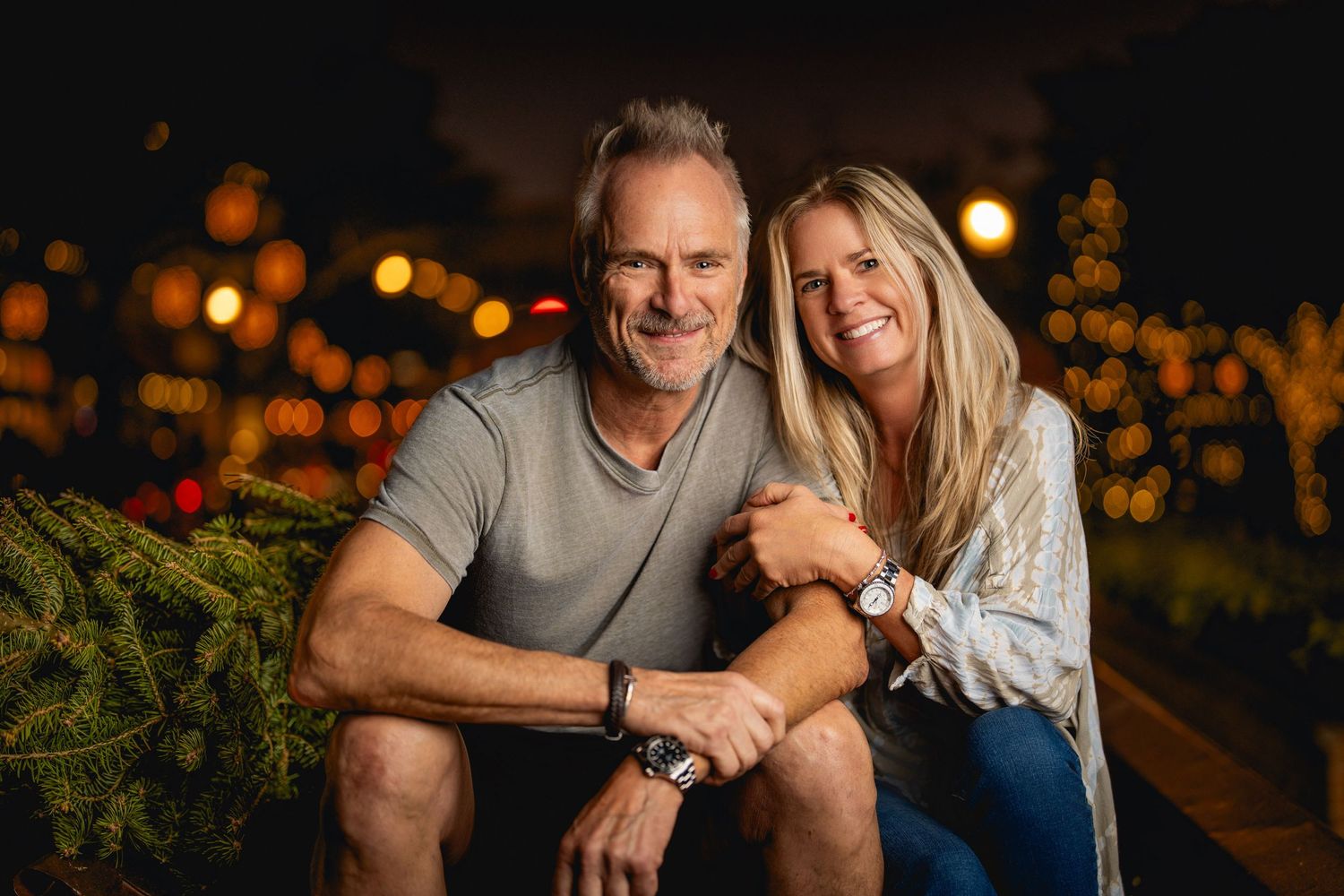 Two people in casual attire sit together on a bench at dusk with bokeh lights glowing in the background.