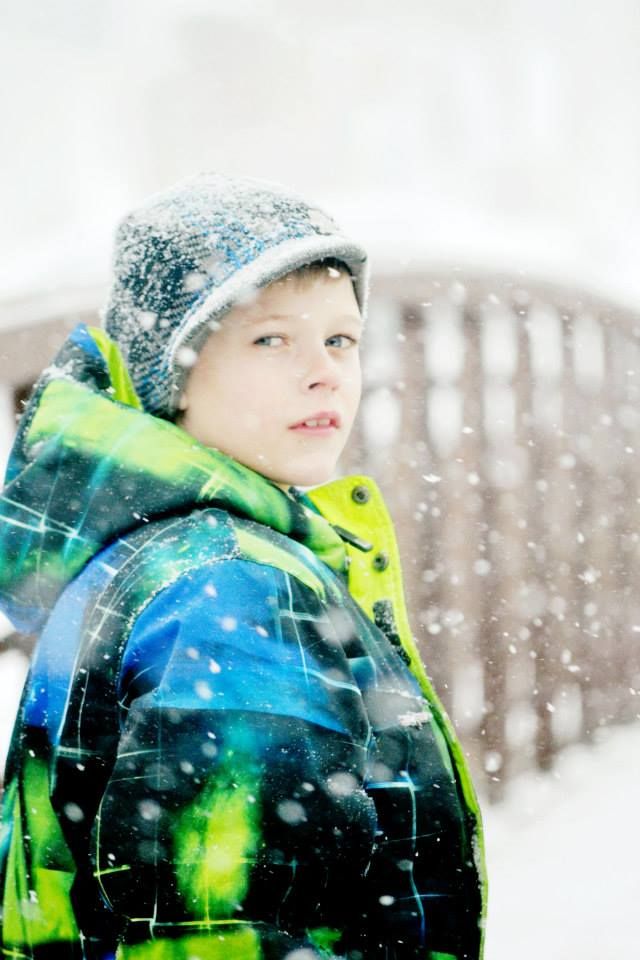A winter portrait showing a person in a bright neon winter coat and knit hat during snowfall.