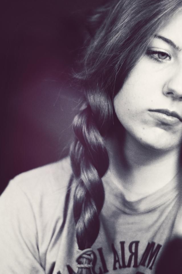 Portrait in black and white style showing a long side braid, partial face view, and casual shirt.