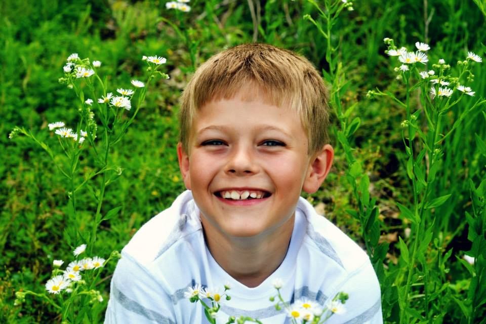 A cheerful portrait in a field of blooming white daisies and lush green plants on a sunny day.
