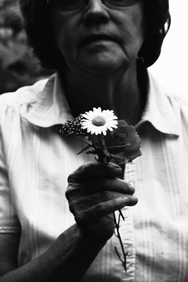 A black and white close-up photo of hands holding a daisy flower against a light background.