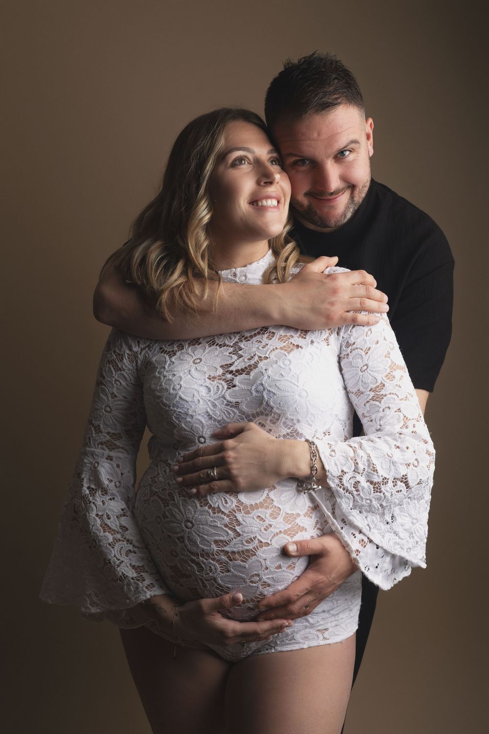 Intimate maternity photoshoot series showing couple in white lace against dark background.