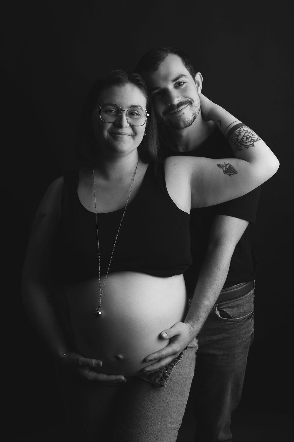 A series of intimate black and white maternity photos showing a pregnant belly and partner in dim lighting.