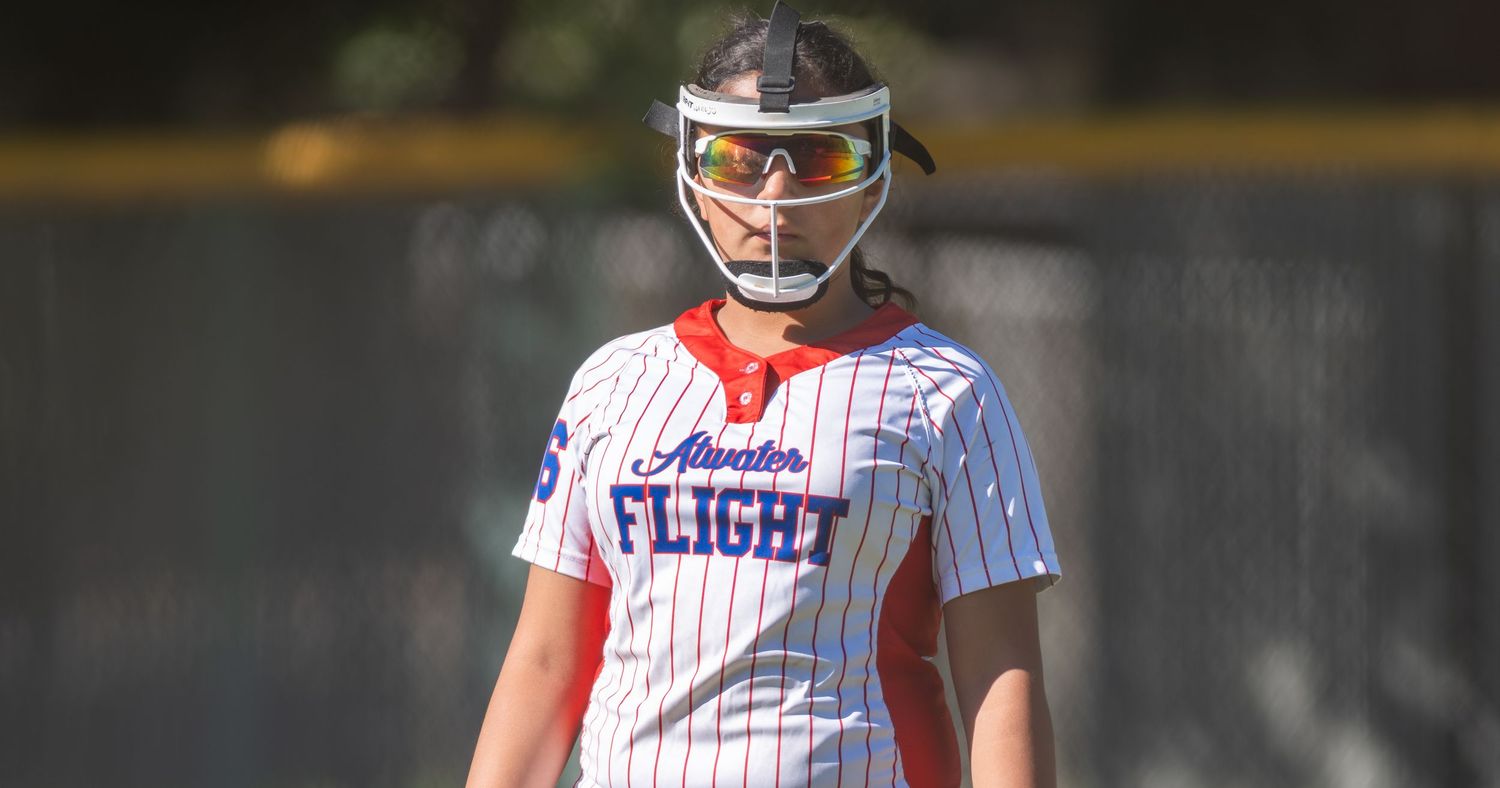 Softball player in Atlantic Flight uniform wearing helmet and sunglasses on sunny field.