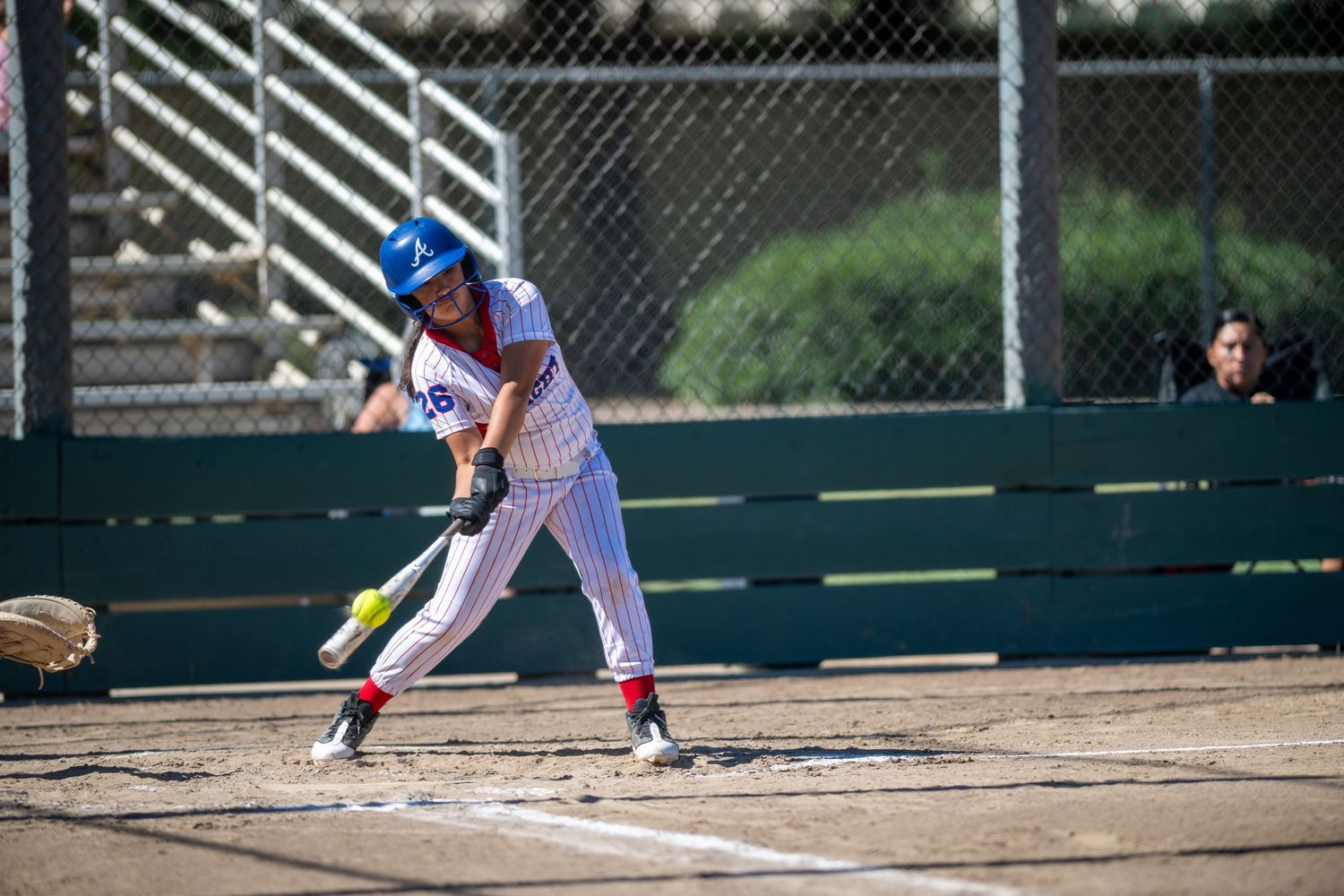 Female softball player in blue helmet and pinstripe uniform preparing to bat during a sunny outdoor game.