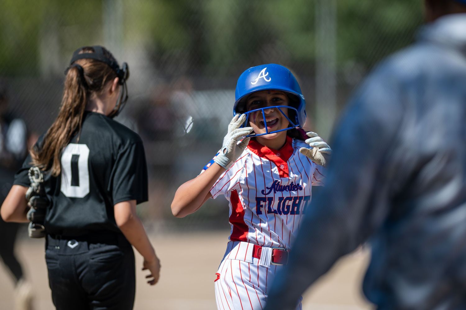 Young softball player in Arizona Flight uniform celebrates on base during a sunny outdoor game.