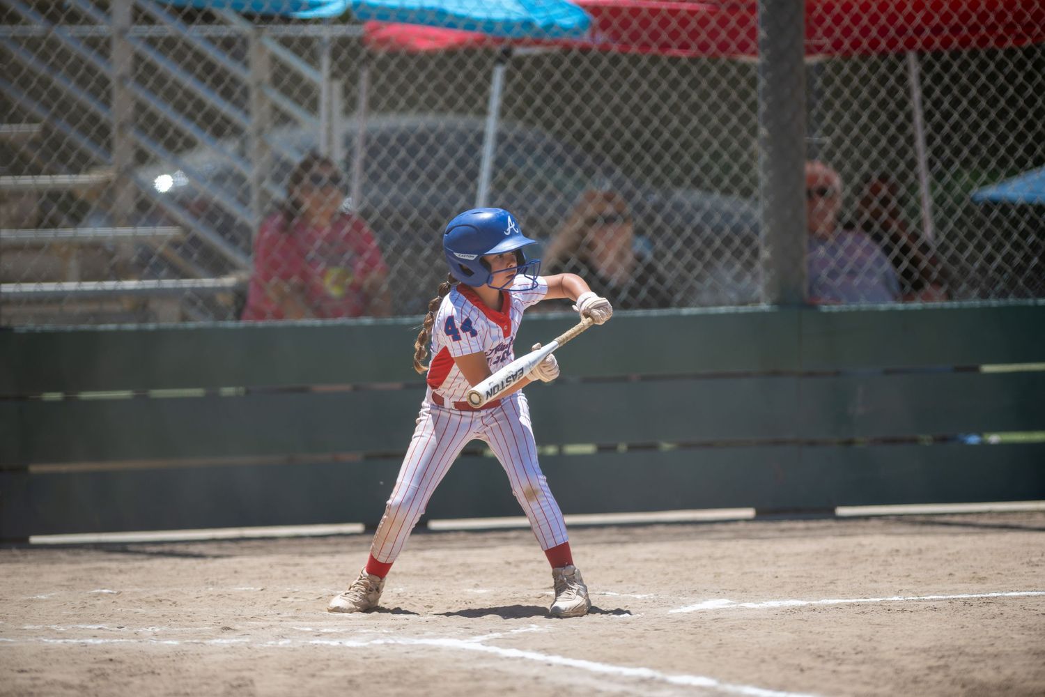 Young baseball player in red and white uniform batting at home plate during a sunny youth league game.
