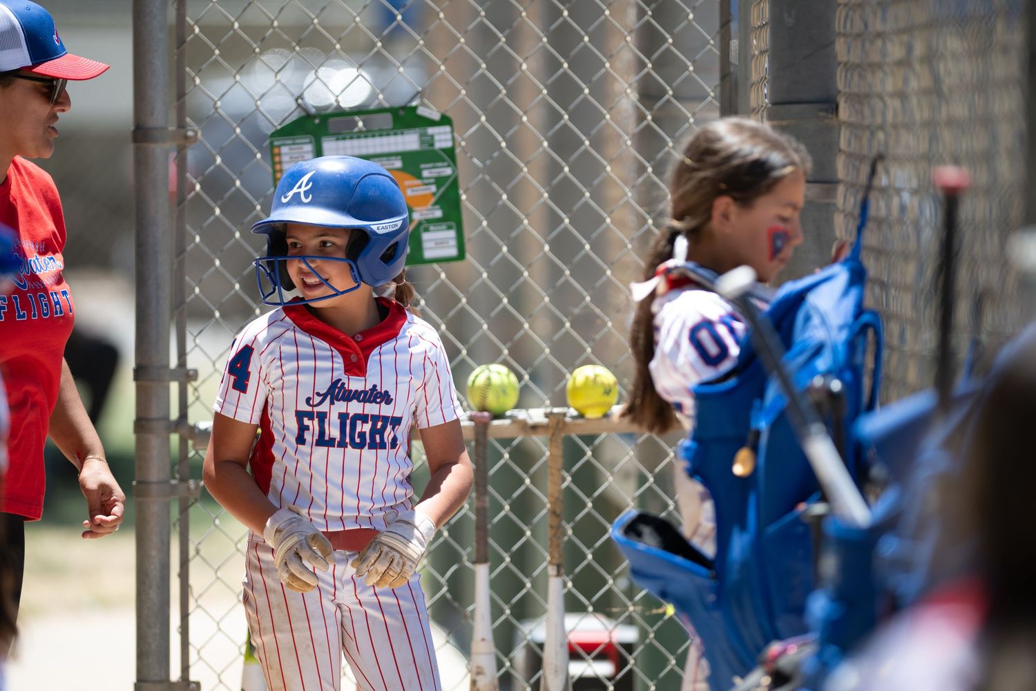 Young softball player in Georgia Flight uniform smiling near dugout fence during a youth softball game.