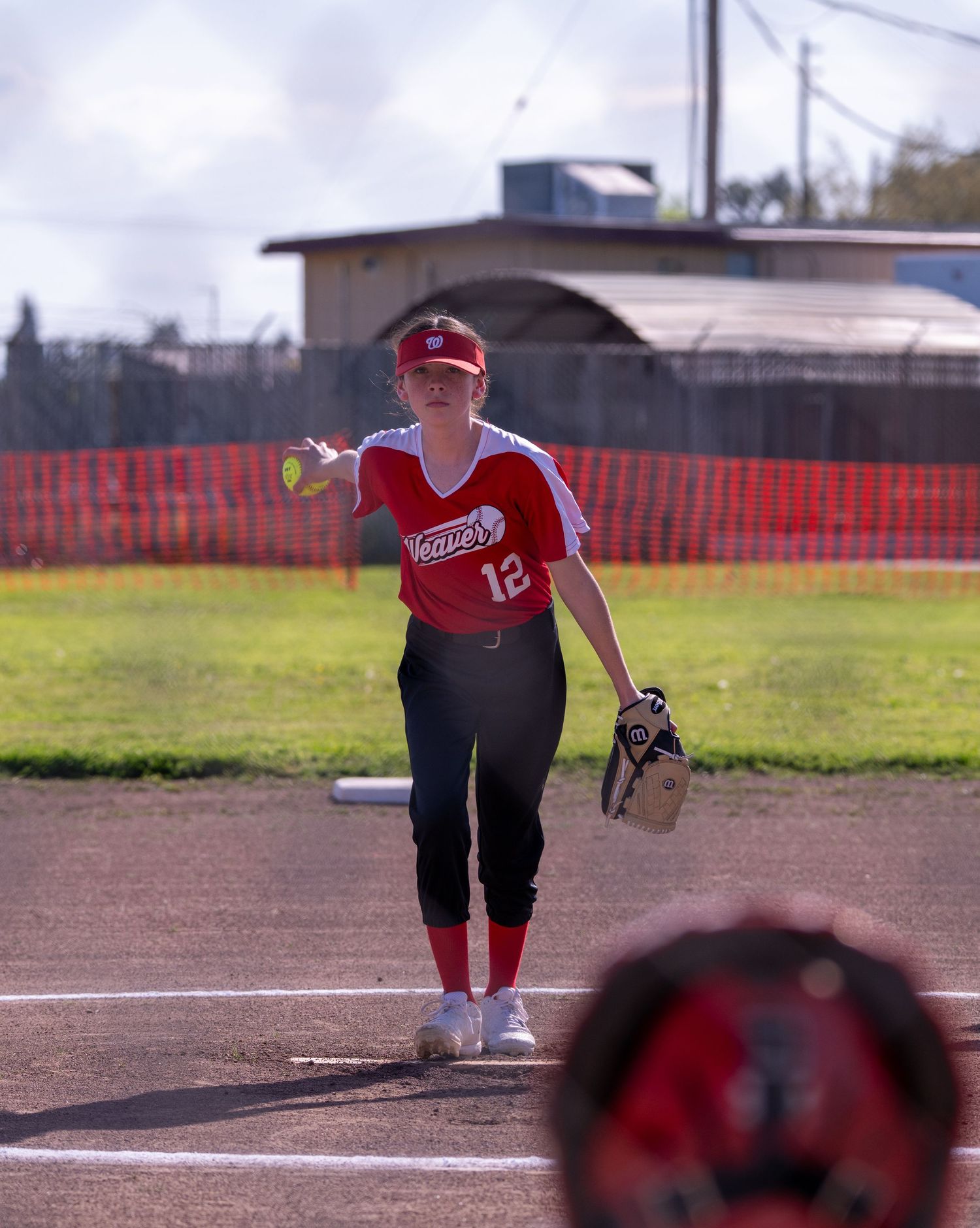 Softball player in red jersey practicing pitching form on dirt field.