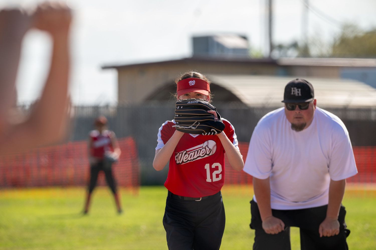 Softball players in red and blue uniforms practicing on a sunny field during a game.