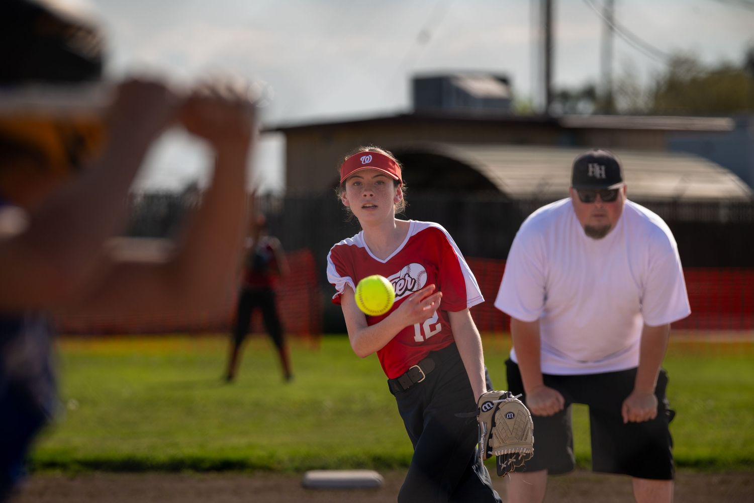 Softball player in red uniform pitching yellow ball during practice.