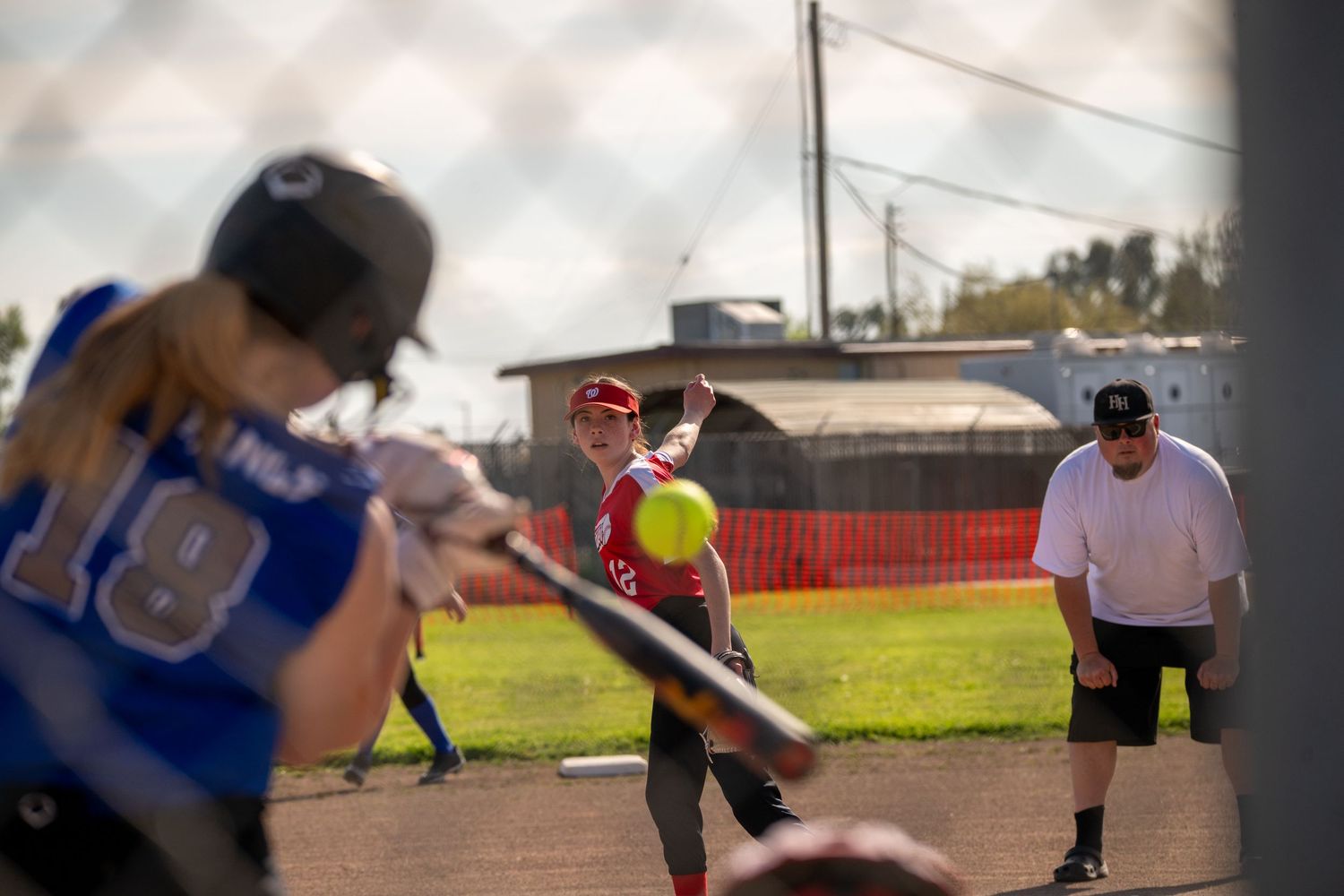 Players positioned across the softball field during a game with red uniforms visible.