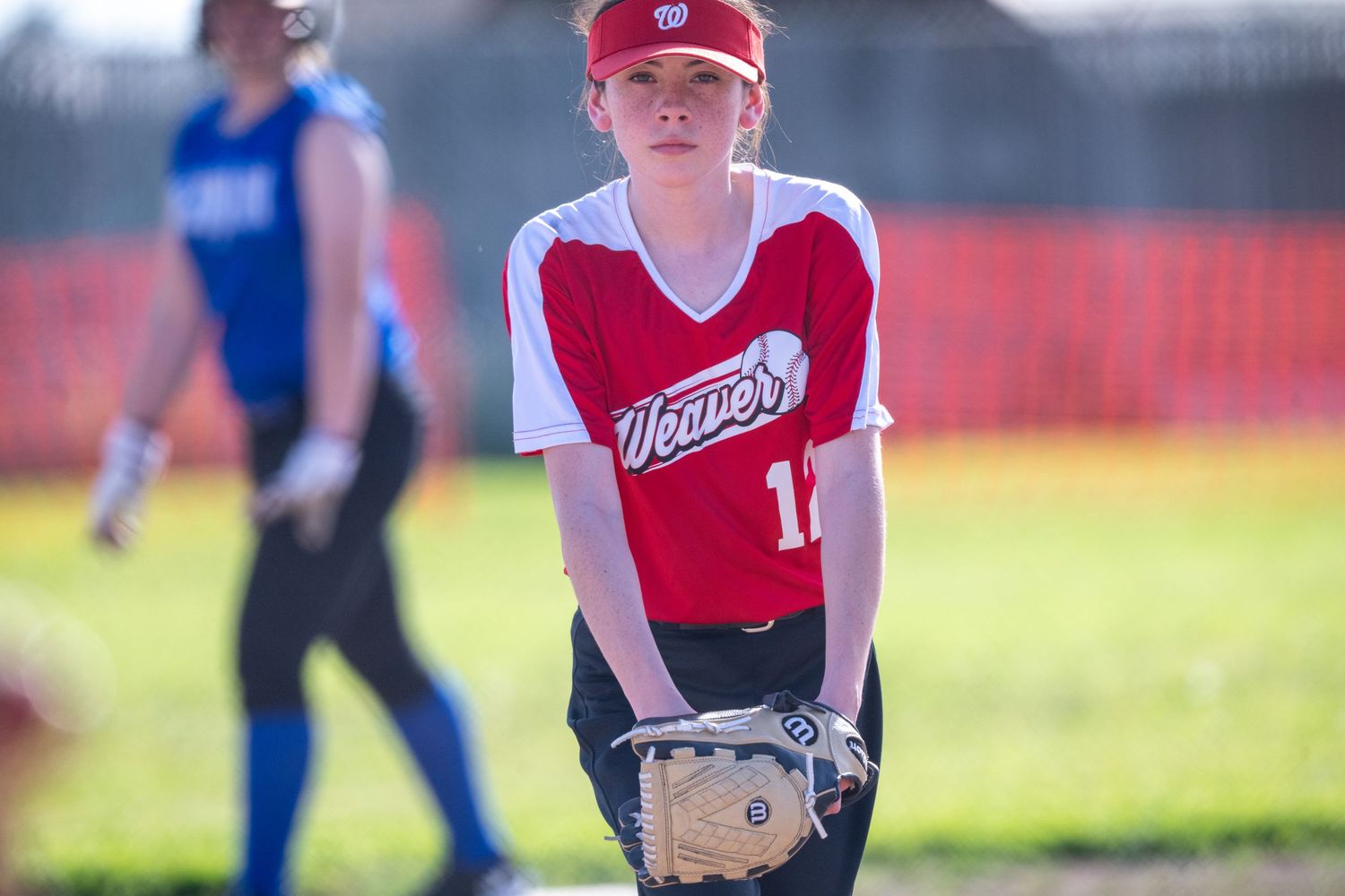 Softball athletes from opposing teams engaged in gameplay on a grass field.