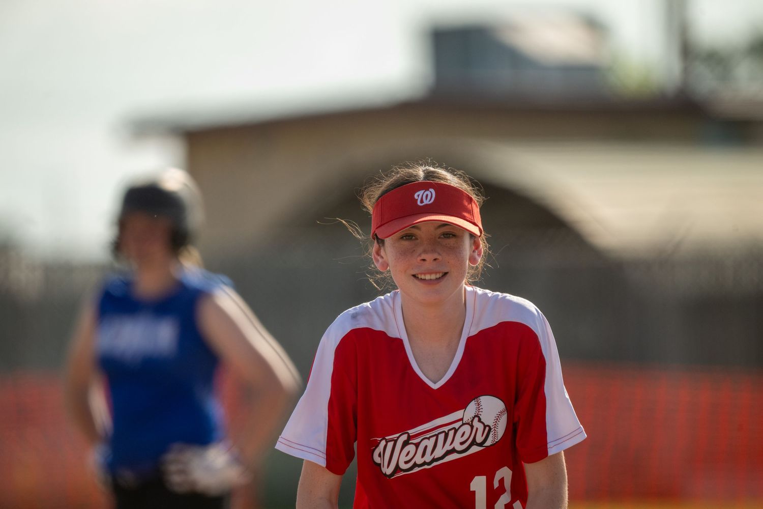 Players in red team uniforms ready their positions during a softball match.