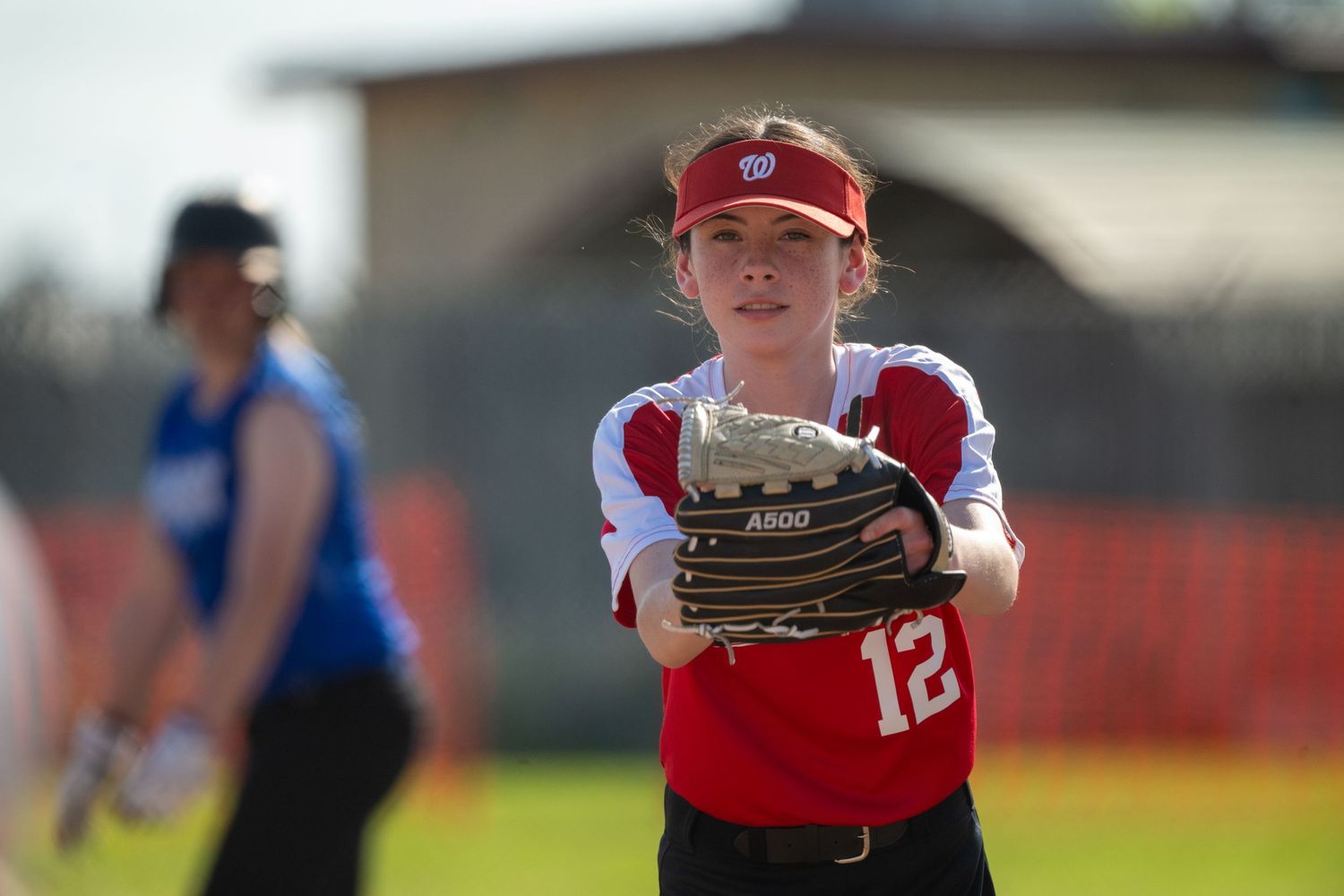 Softball player in red uniform positioned defensively on field during game action.