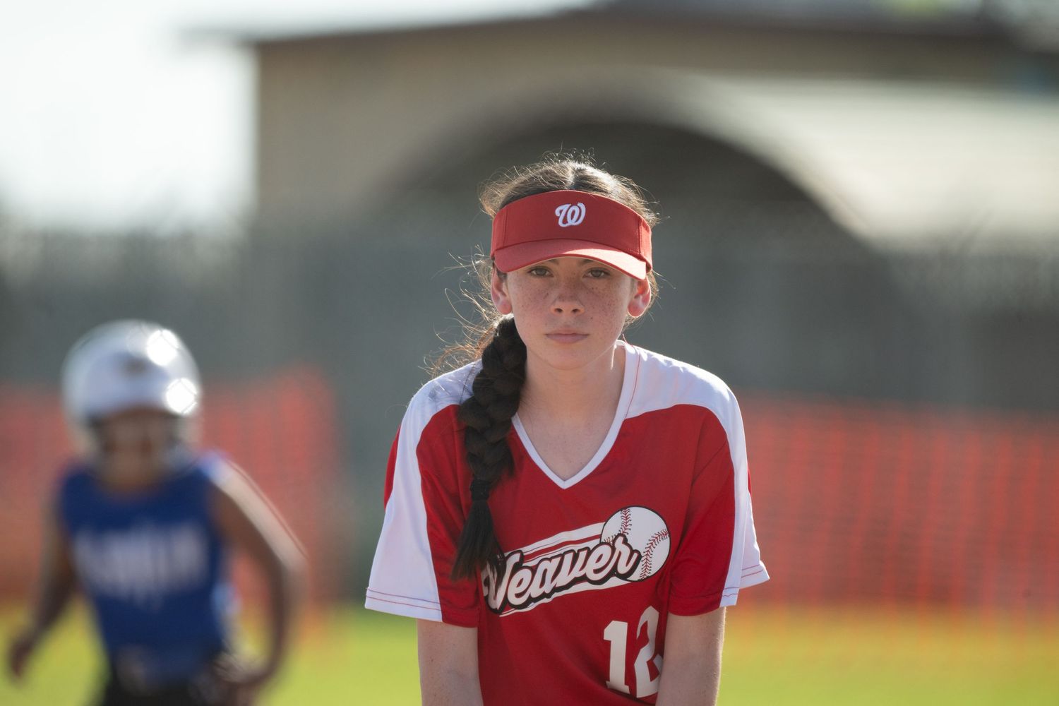 Team members in red jerseys prepare for play during afternoon softball game.