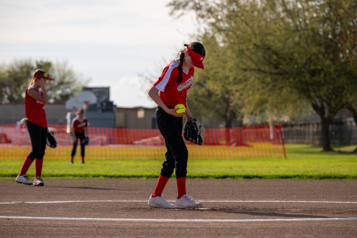 Wide shot of softball field showing players spread out during game action.