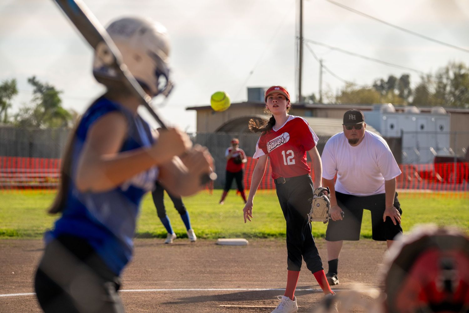 Action shot of softball game showing players from red and blue teams on field.
