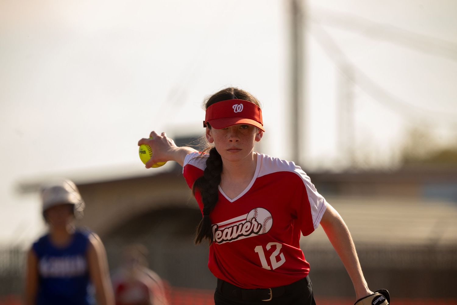 A softball pitcher in a red uniform releases a pitch during a competitive game.