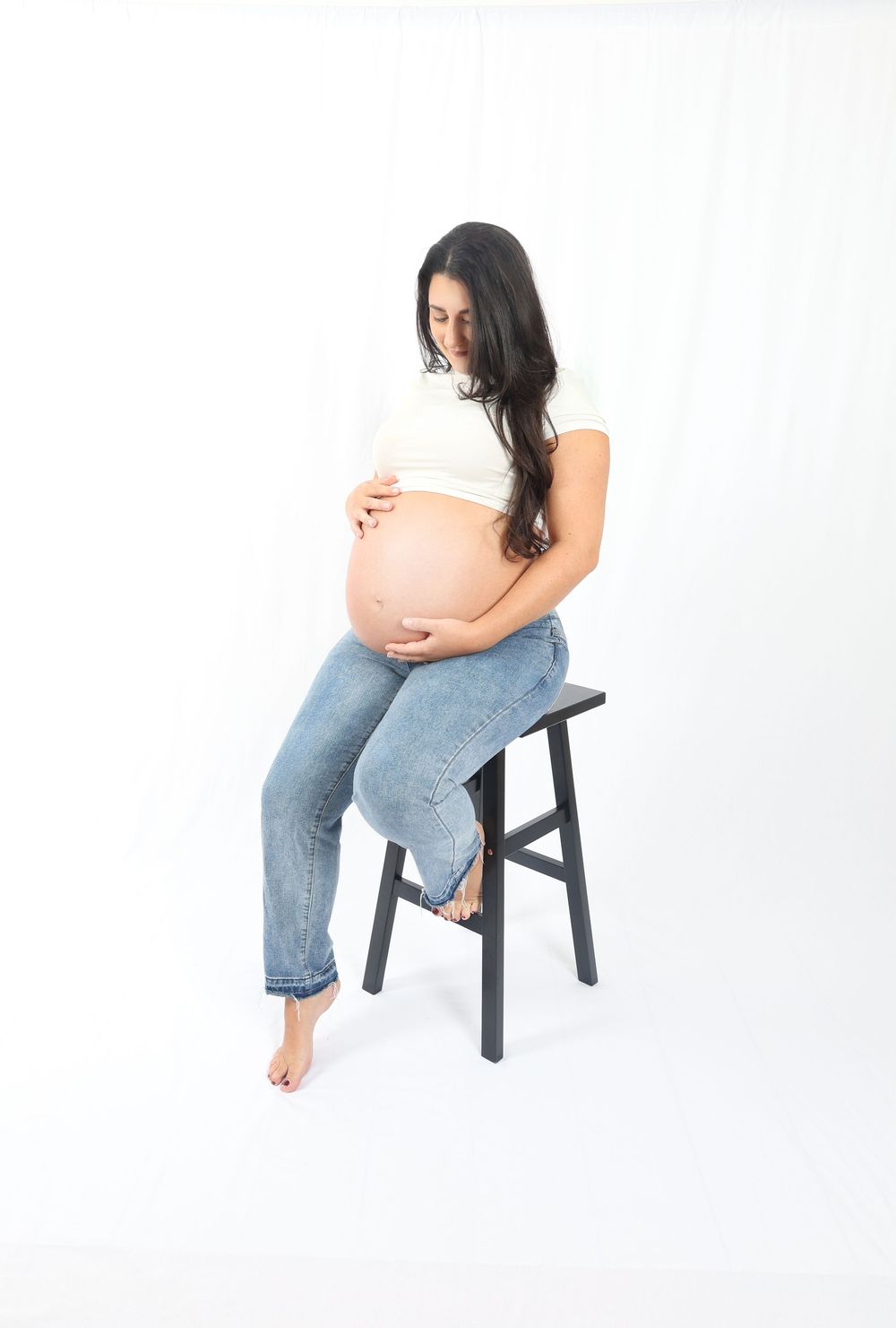 A series of maternity poses on a black stool against a white backdrop.