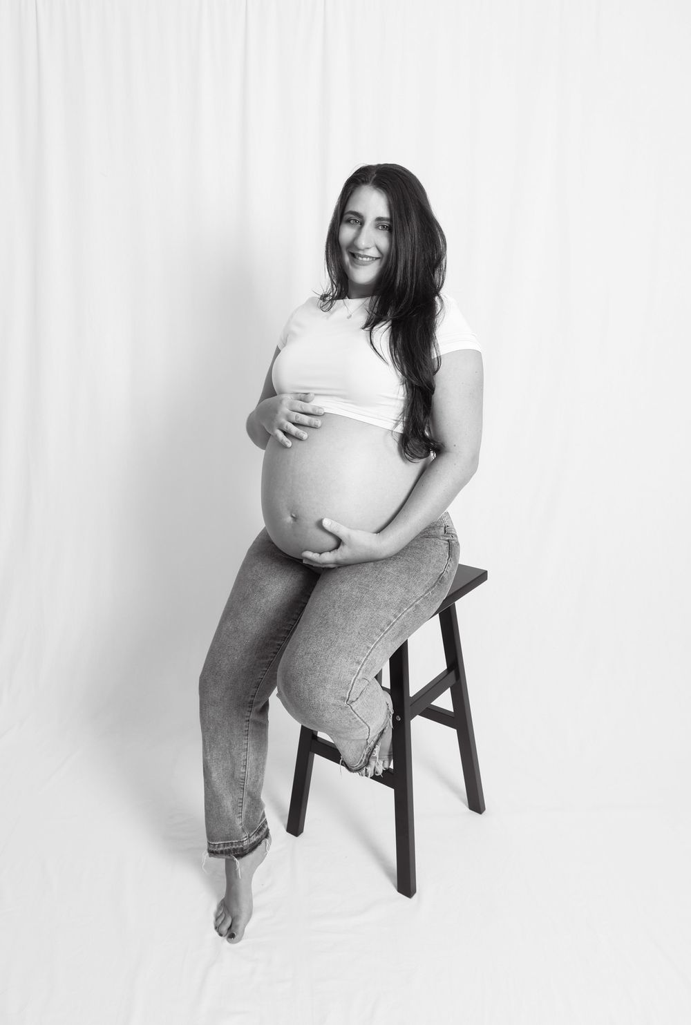 Minimalist black and white maternity portraits with wooden chair against white background.