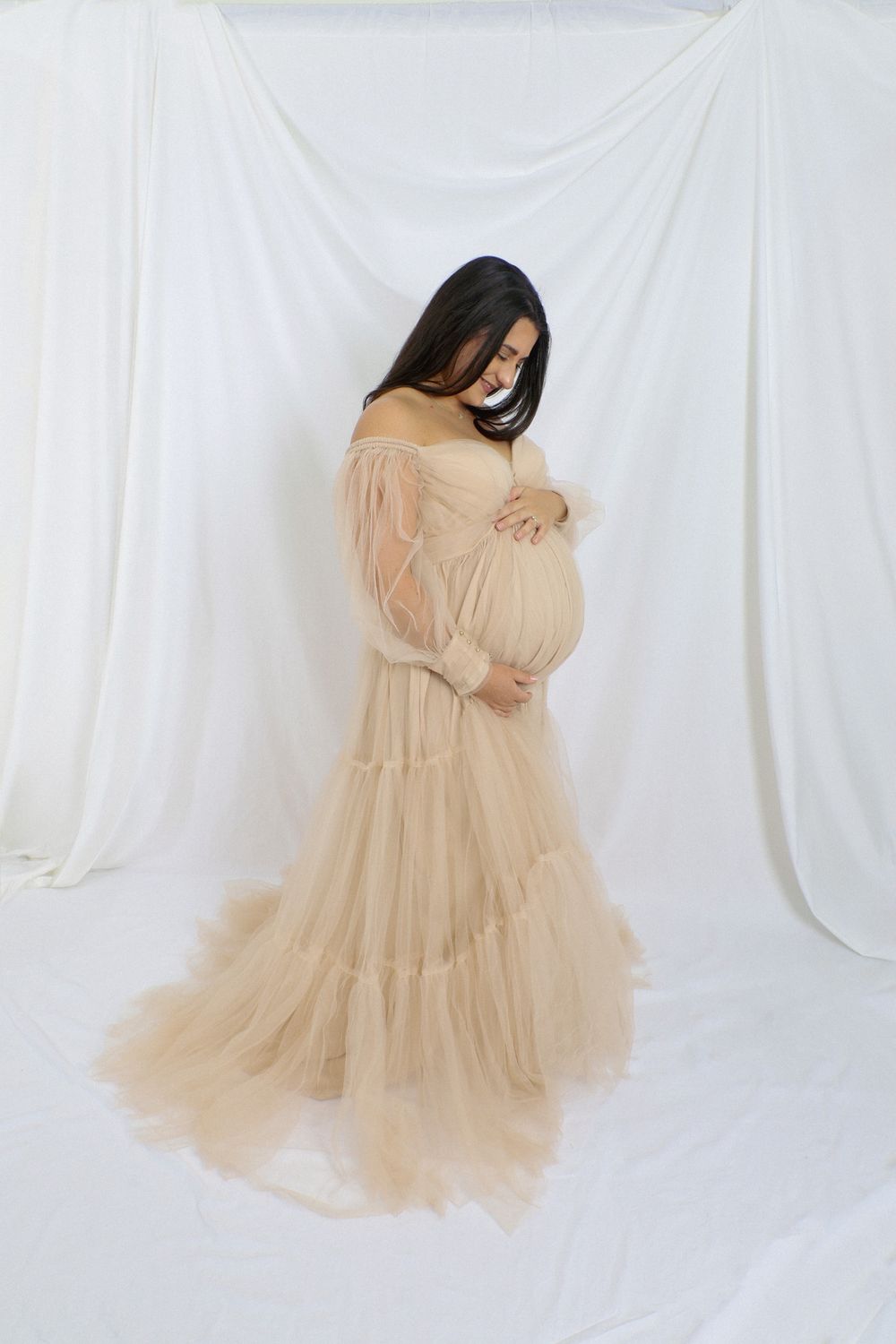 Flowing beige tulle maternity gown portraits against clean white backdrop.