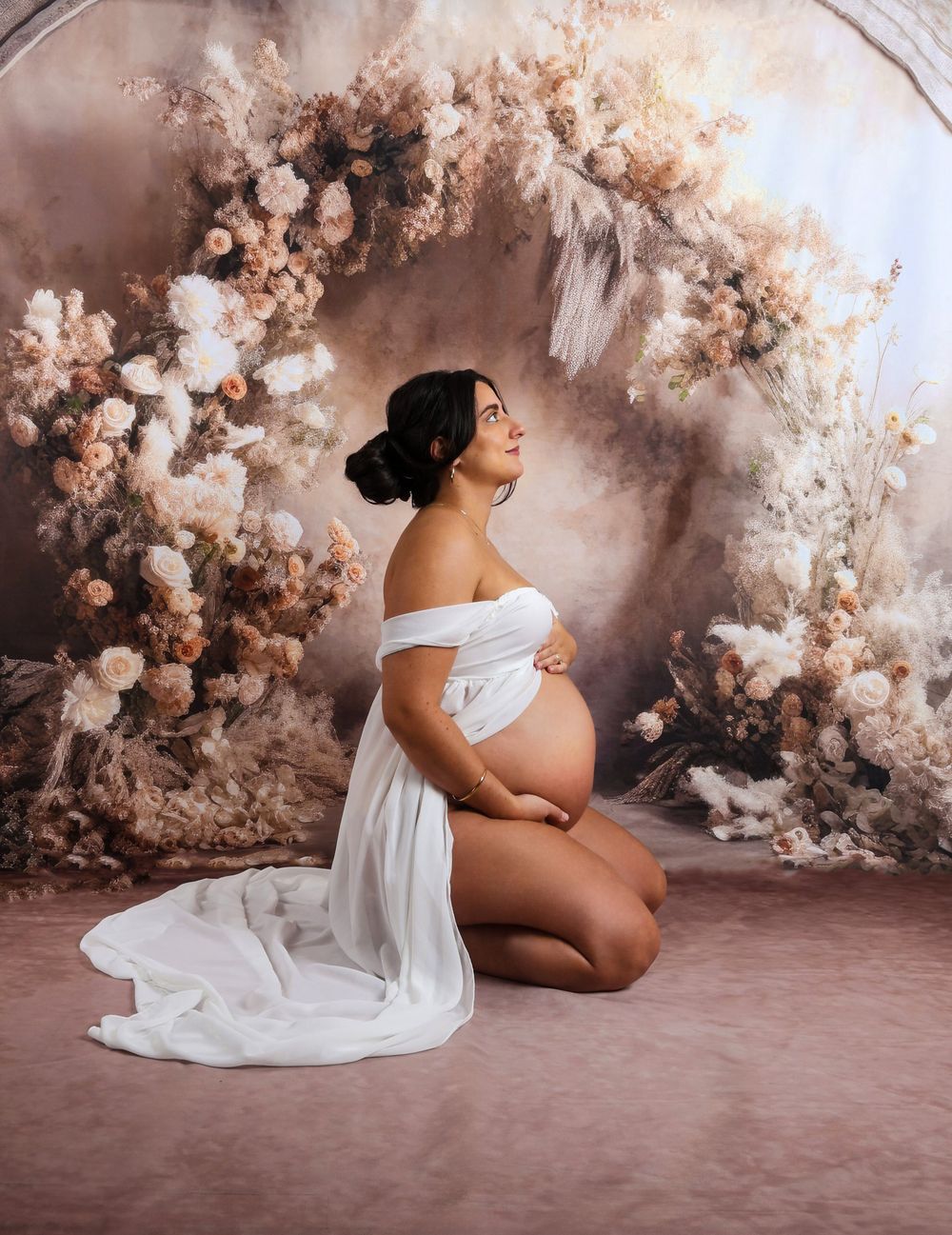 Artistic maternity portraits surrounded by pink cherry blossoms and soft lighting.