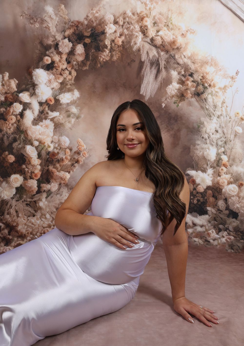 Elegant maternity photos in silver dress against romantic blush floral background.
