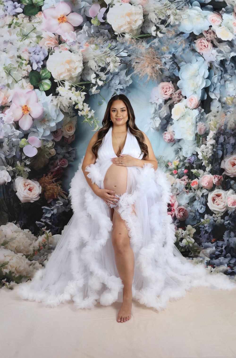 Dreamy maternity session with white tulle against floral wall backdrop.