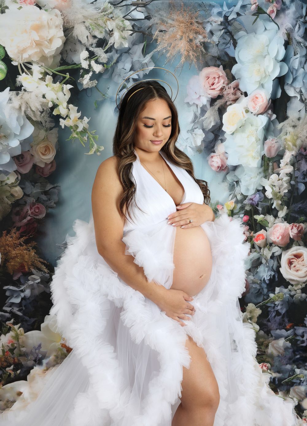 Romantic maternity portraits with white draping and luxurious floral backdrop.