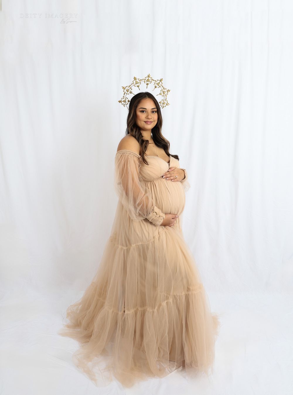 Dreamy maternity portraits with a gold crown and beige tulle dress in a studio setting.